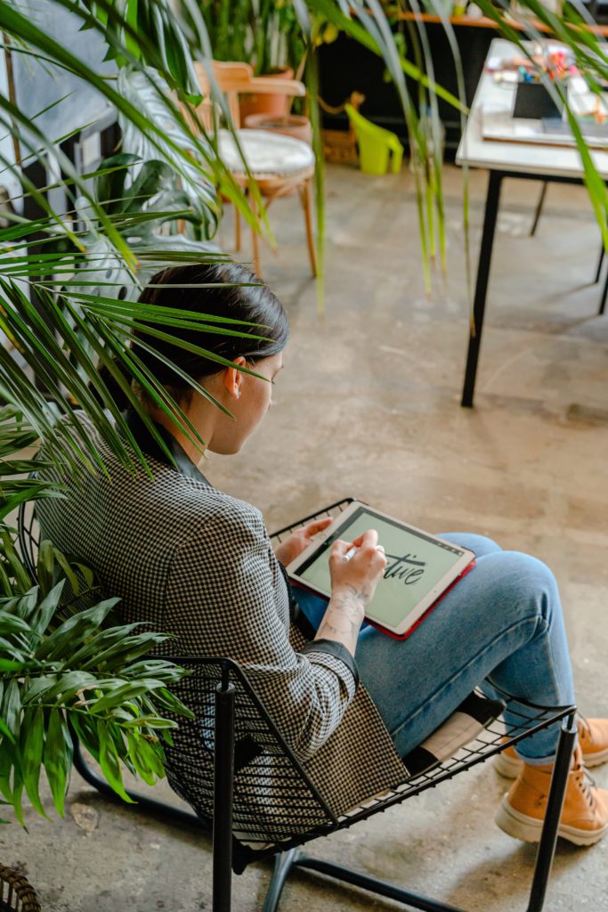woman sitting in a chair working on a tablet with the word create on it